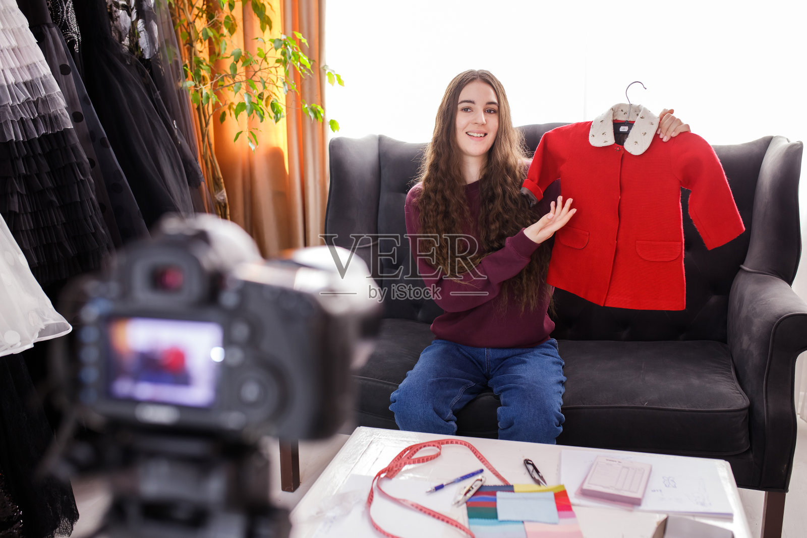 微笑的年轻女子正在拍摄服装评论视频，坐在家里的沙发上。照片摄影图片