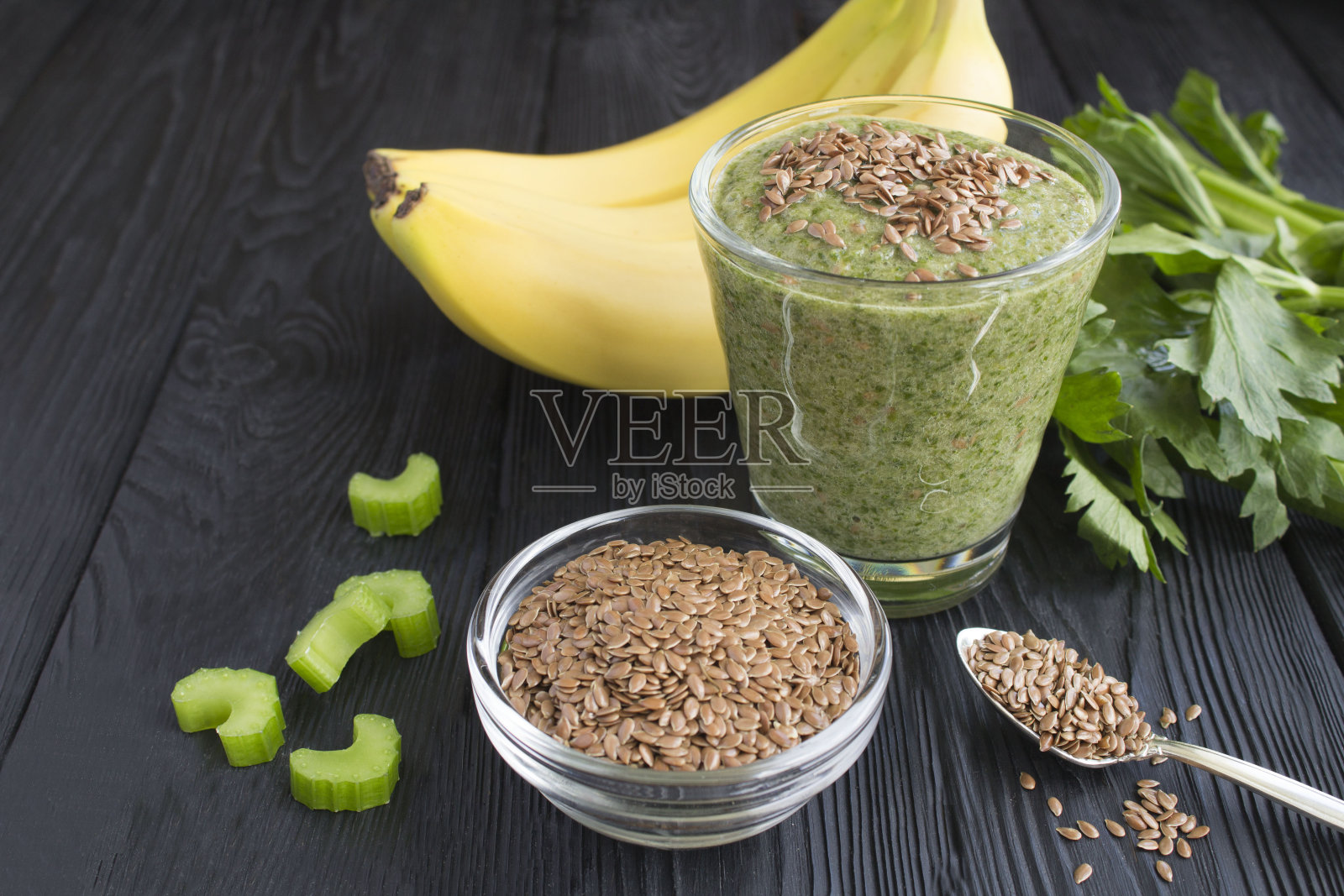 冰沙与亚麻籽，芹菜和香蕉在玻璃上的黑色木制背景。特写镜头。照片摄影图片