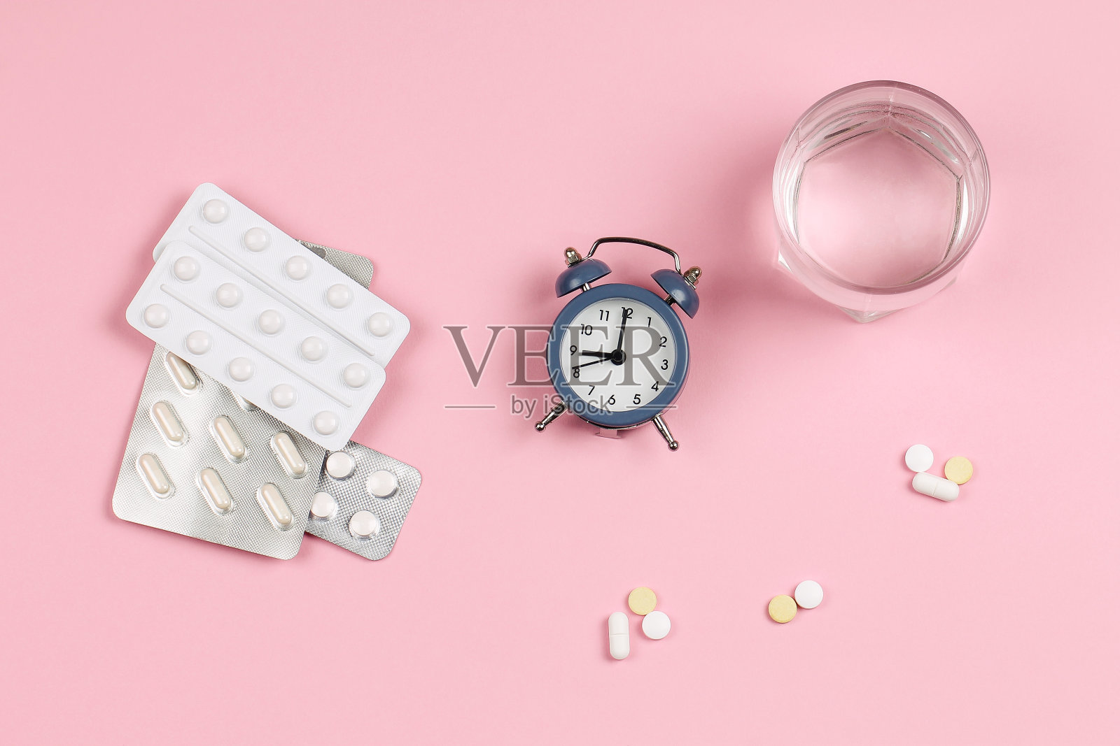 闹钟，一杯水，粉色背景上的药片。照片摄影图片