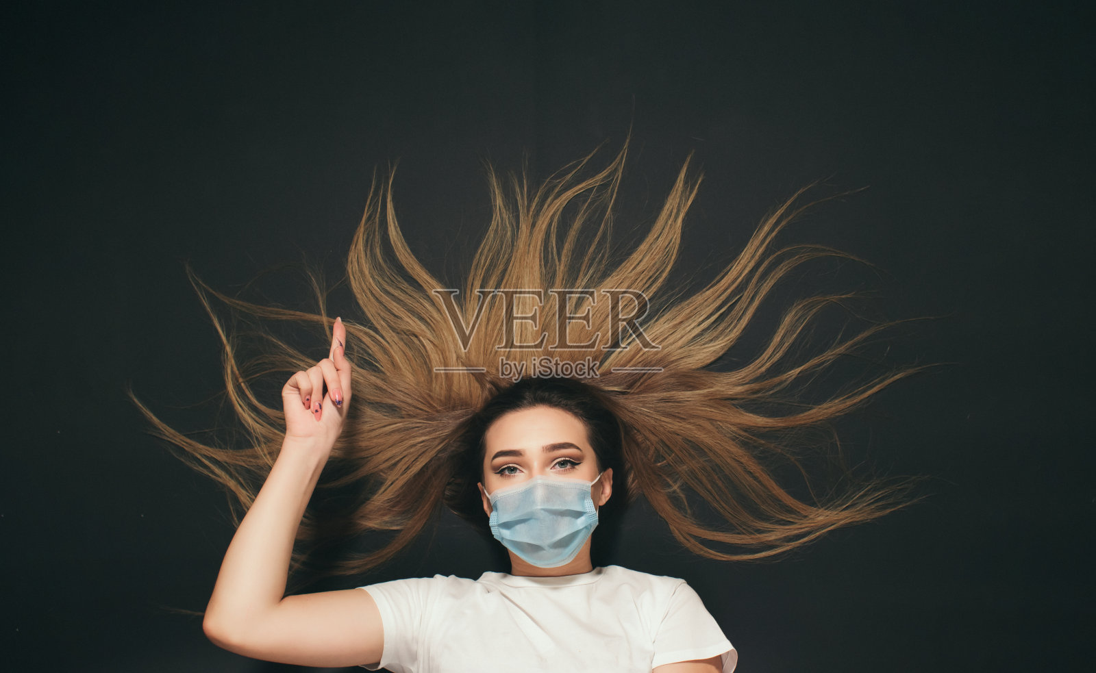 在黑色演播室背景俯视图上，年轻女子戴着防护医用口罩，女孩竖起一根手指宣布照片摄影图片