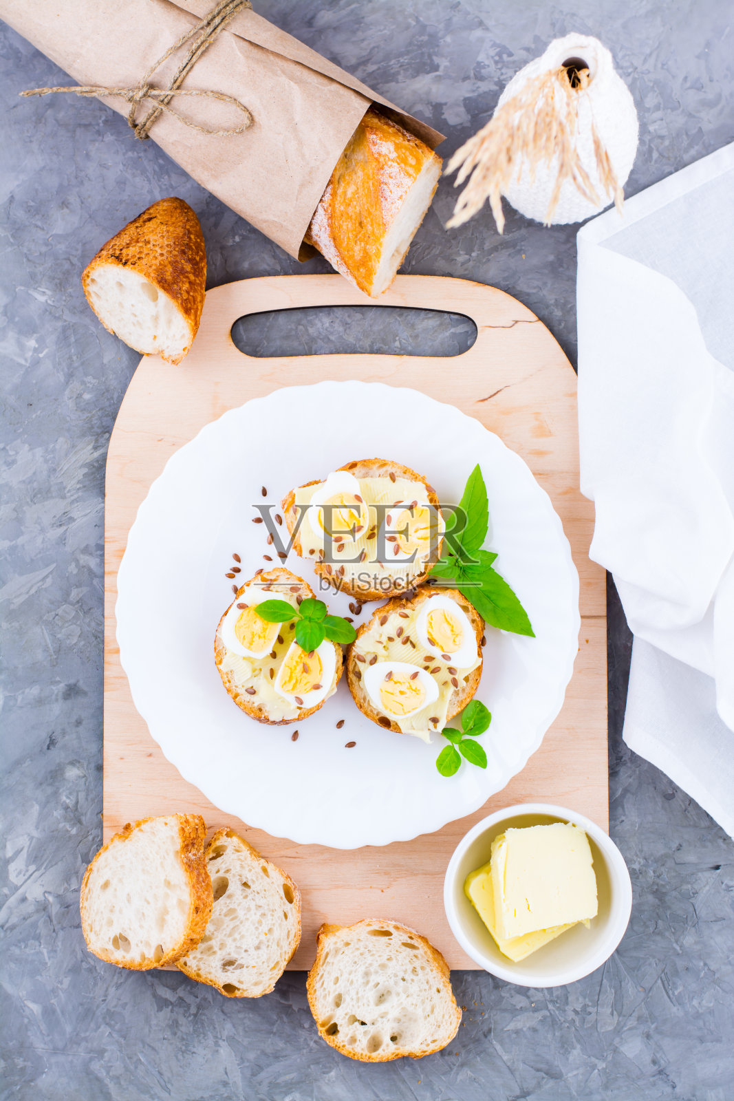 丰盛的早餐。新鲜的法棍三明治，黄油，鹌鹑蛋，亚麻籽和罗勒籽放在桌上的盘子里。顶部和垂直视图照片摄影图片