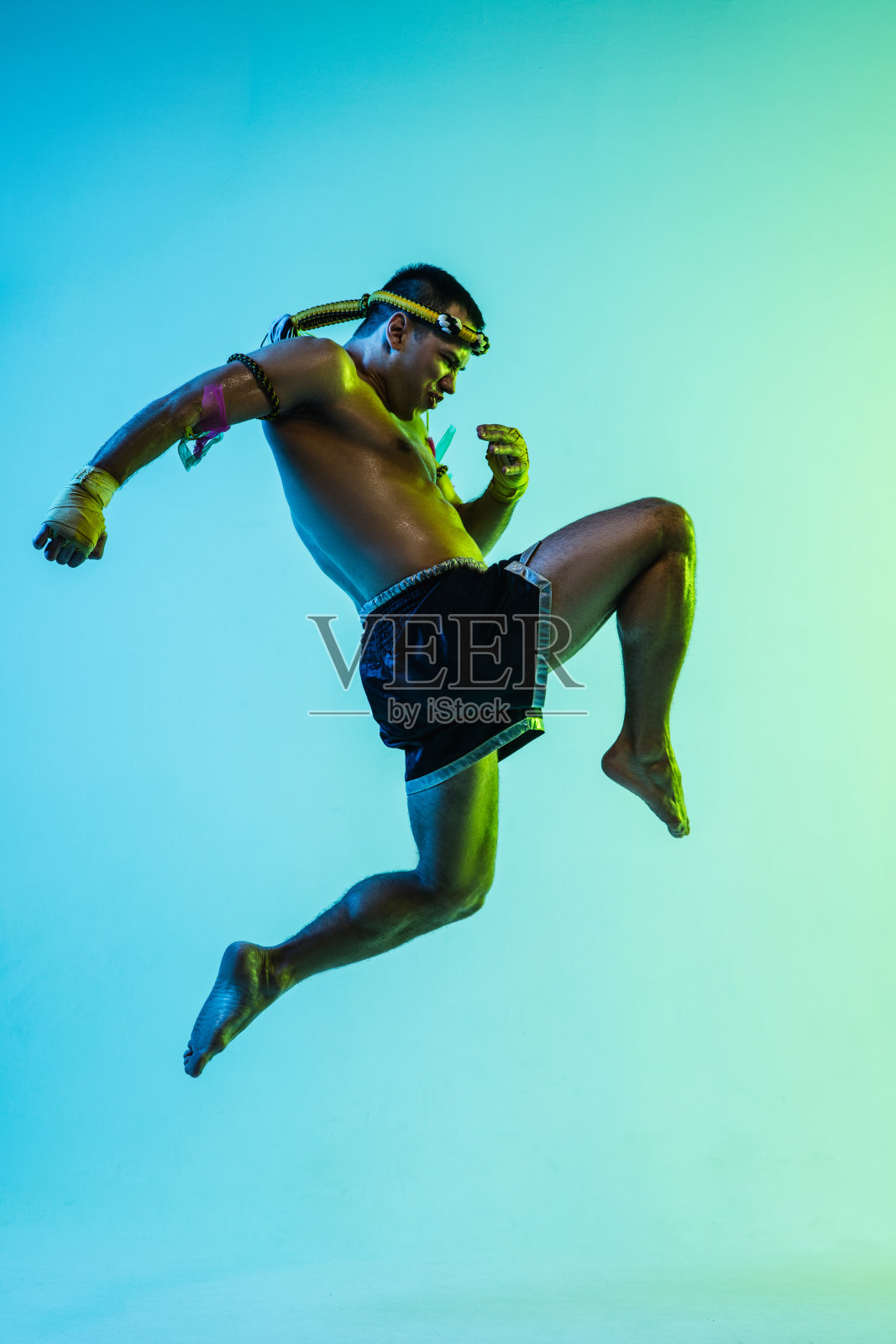 年轻男子泰国拳击手训练在霓虹灯的蓝色背景。照片摄影图片