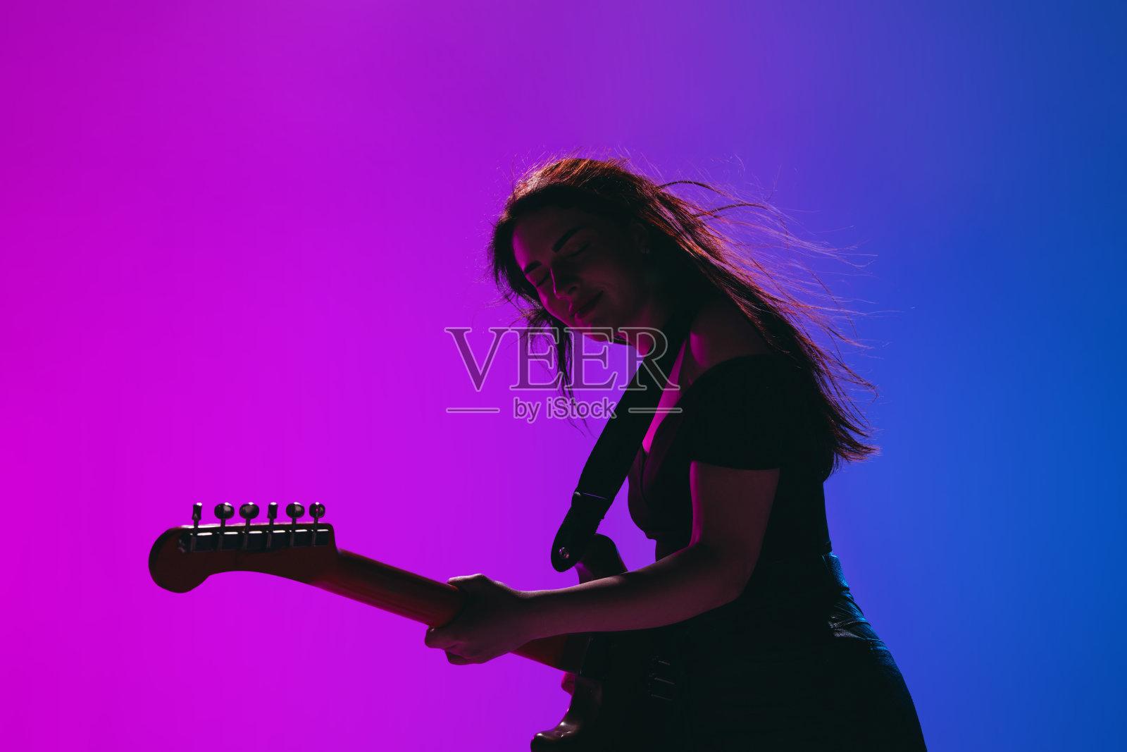 剪影的年轻女吉他手孤立在梯度背景霓虹灯。照片摄影图片