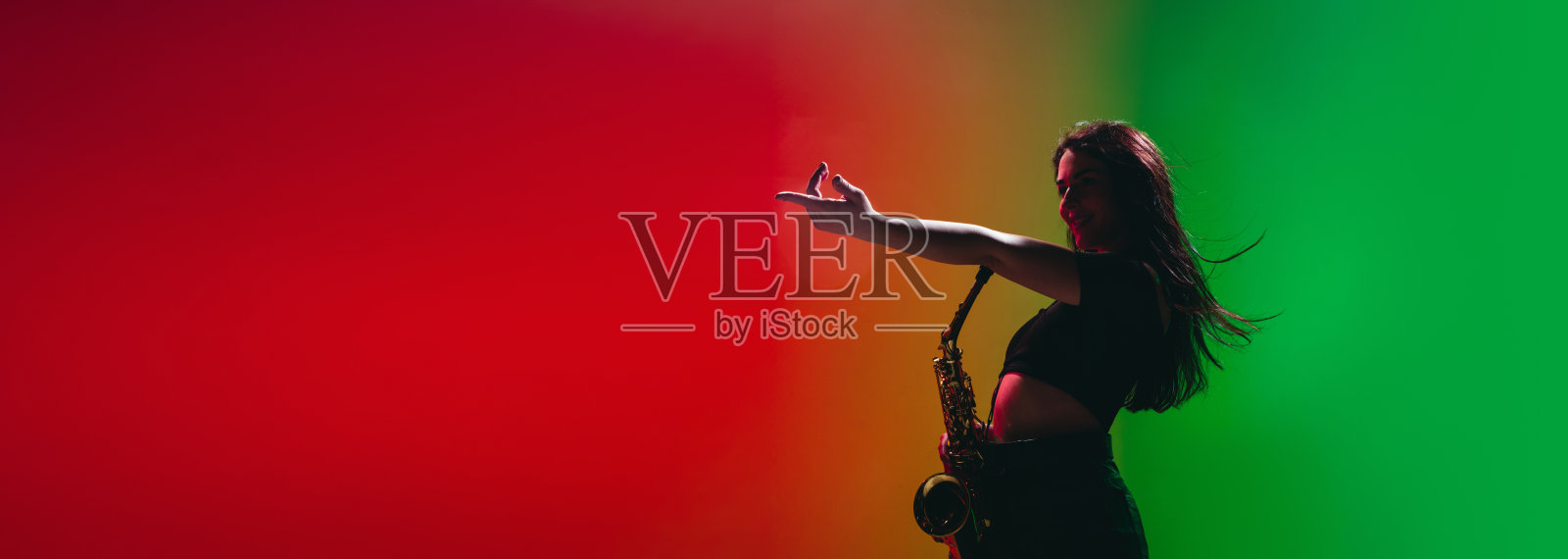 年轻女孩的剪影与萨克斯摆姿势孤立在绿色红色的背景。照片摄影图片