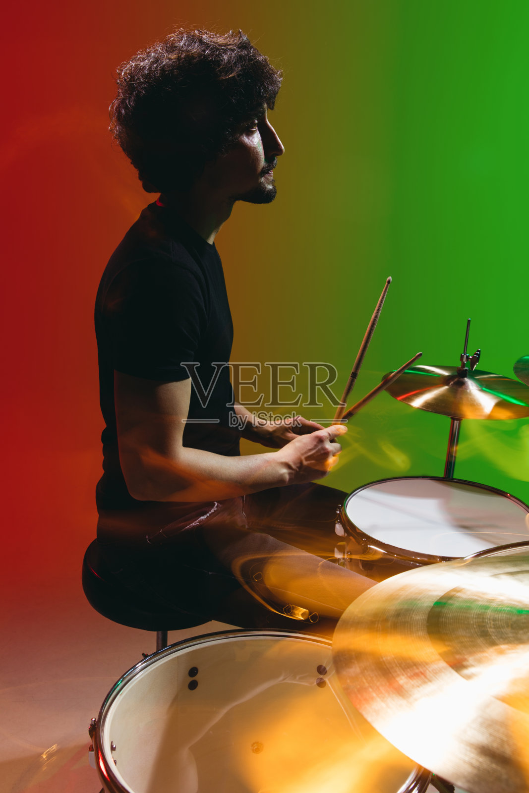 年轻男子鼓手的肖像，在霓虹灯的红绿背景上孤立地演奏照片摄影图片