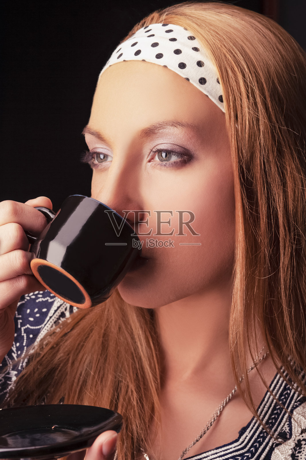 金发女孩的肖像与咖啡杯在黑色的背景。垂直的图像组成照片摄影图片