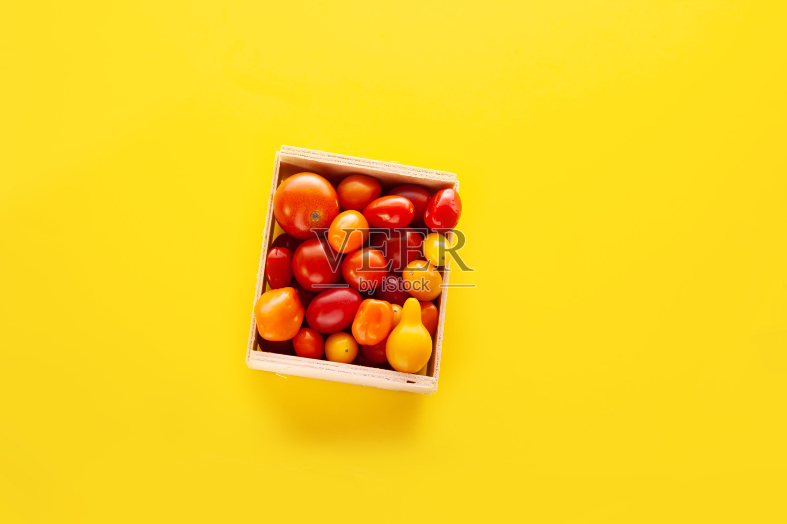 木质的方形盒子里放着新鲜的樱桃番茄，背景是黄色的照片摄影图片
