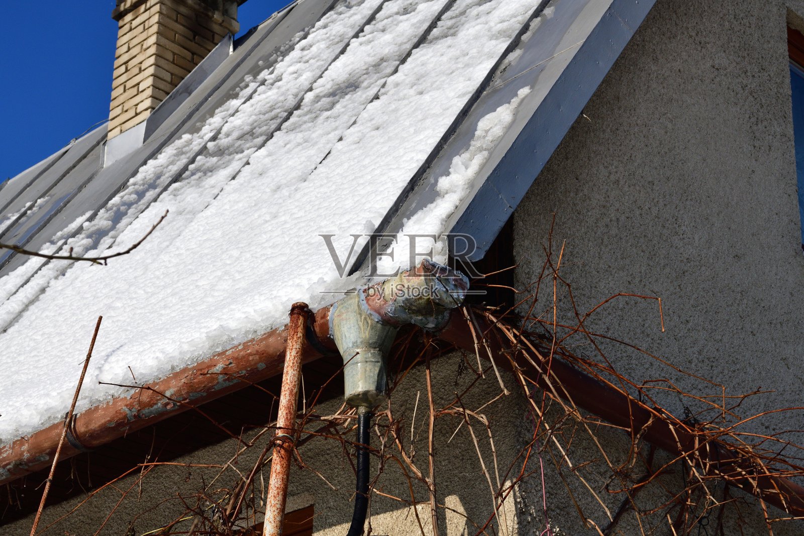 融化的雪通过排水管从屋顶滴落到地面照片摄影图片