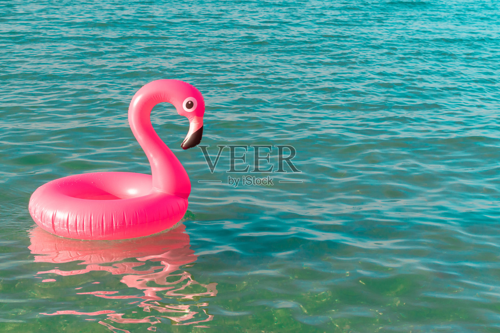 夏天出售。粉红色的充气火烈鸟在蓝色的海水为海夏季海滩的背景。最小的夏天的概念。照片摄影图片