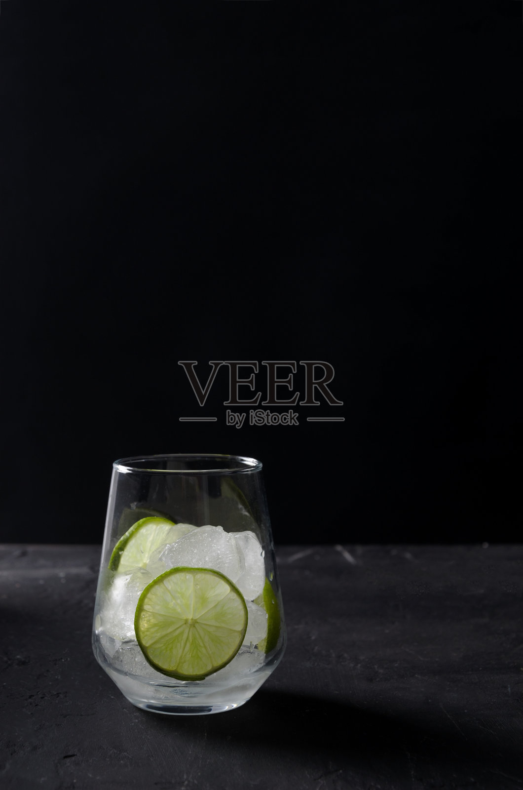 冰在一个透明的玻璃上，一块没有液体的石灰在黑色的背景上，选择焦点照片摄影图片