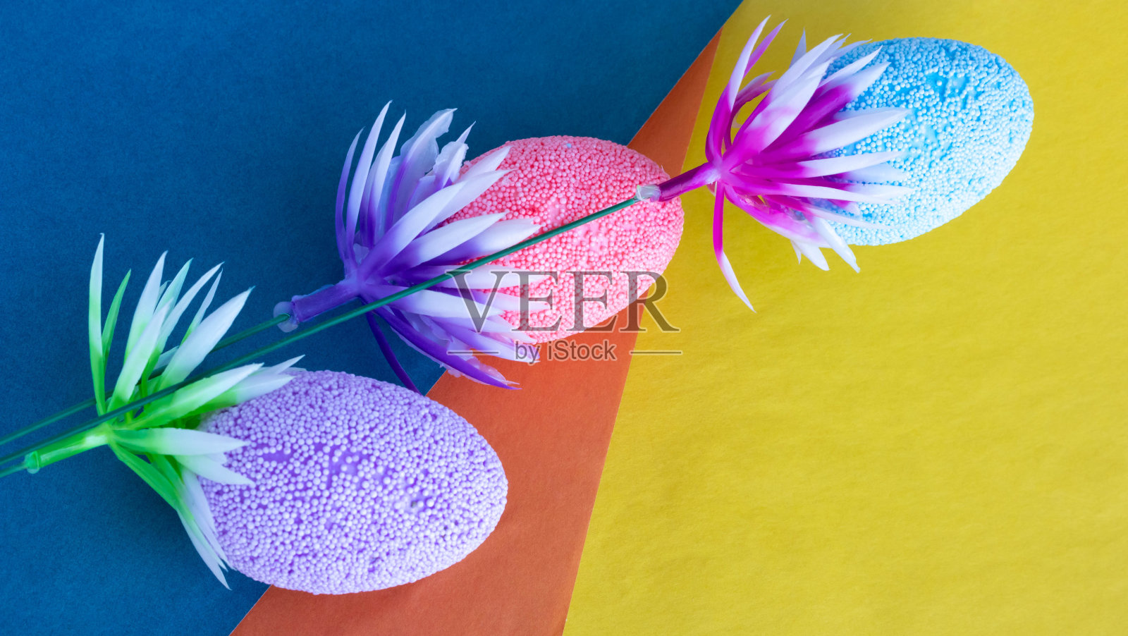 彩色的纸上放着一根带着彩色复活节彩蛋的小树枝。复活节的概念照片摄影图片