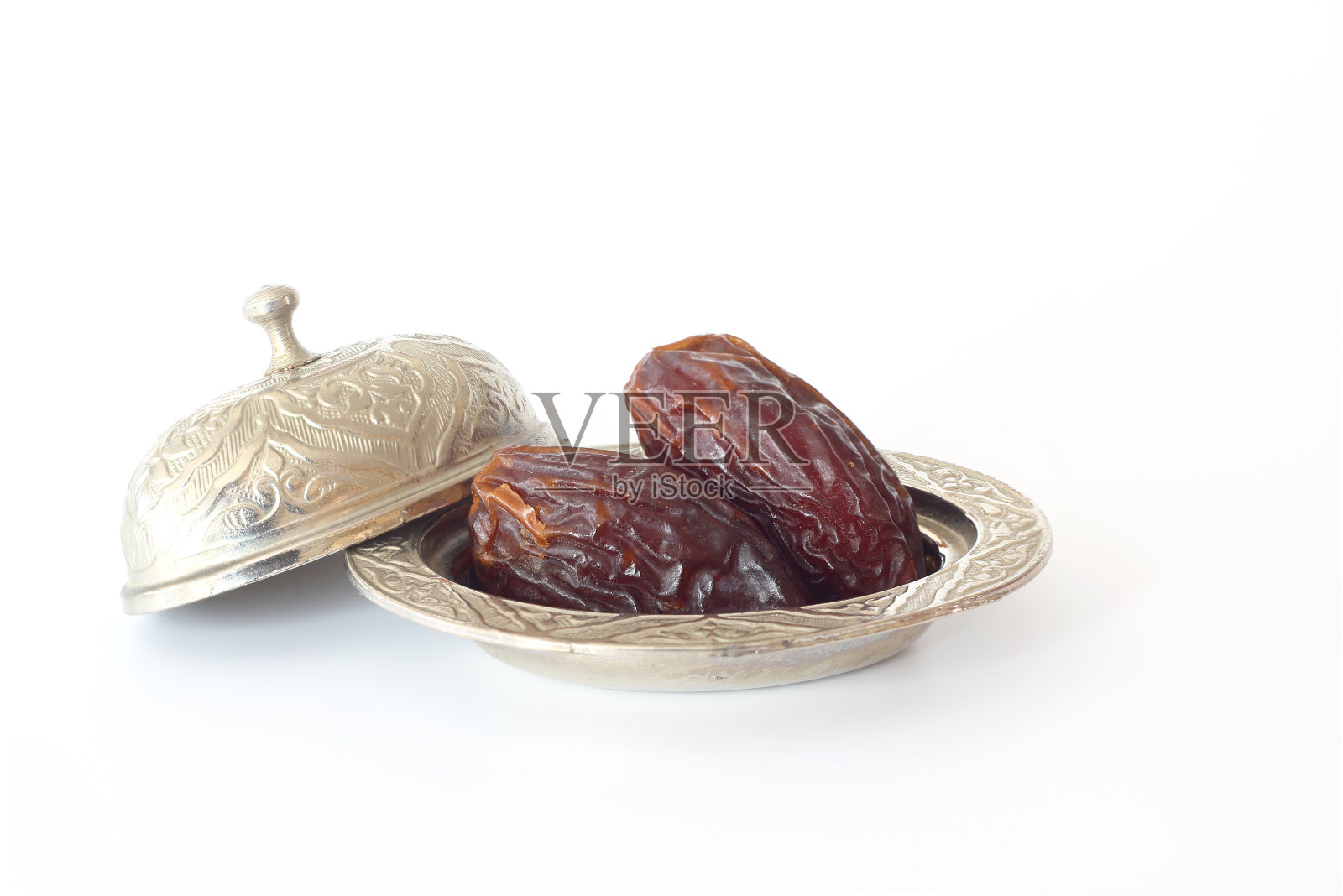 白底银碗里的干棕枣果实。照片摄影图片