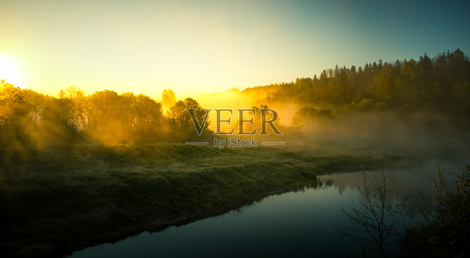 一幅美丽的春景，晨雾缭绕的河谷。春天的景色是一条小河流过森林。水分在阳光下蒸发。照片摄影图片