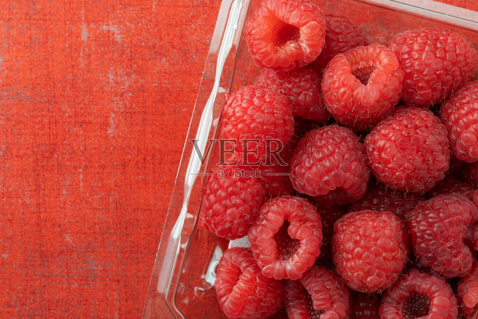 上面近距离观察新鲜采摘的树莓在一个塑料容器在一个橙色的织物背景照片摄影图片