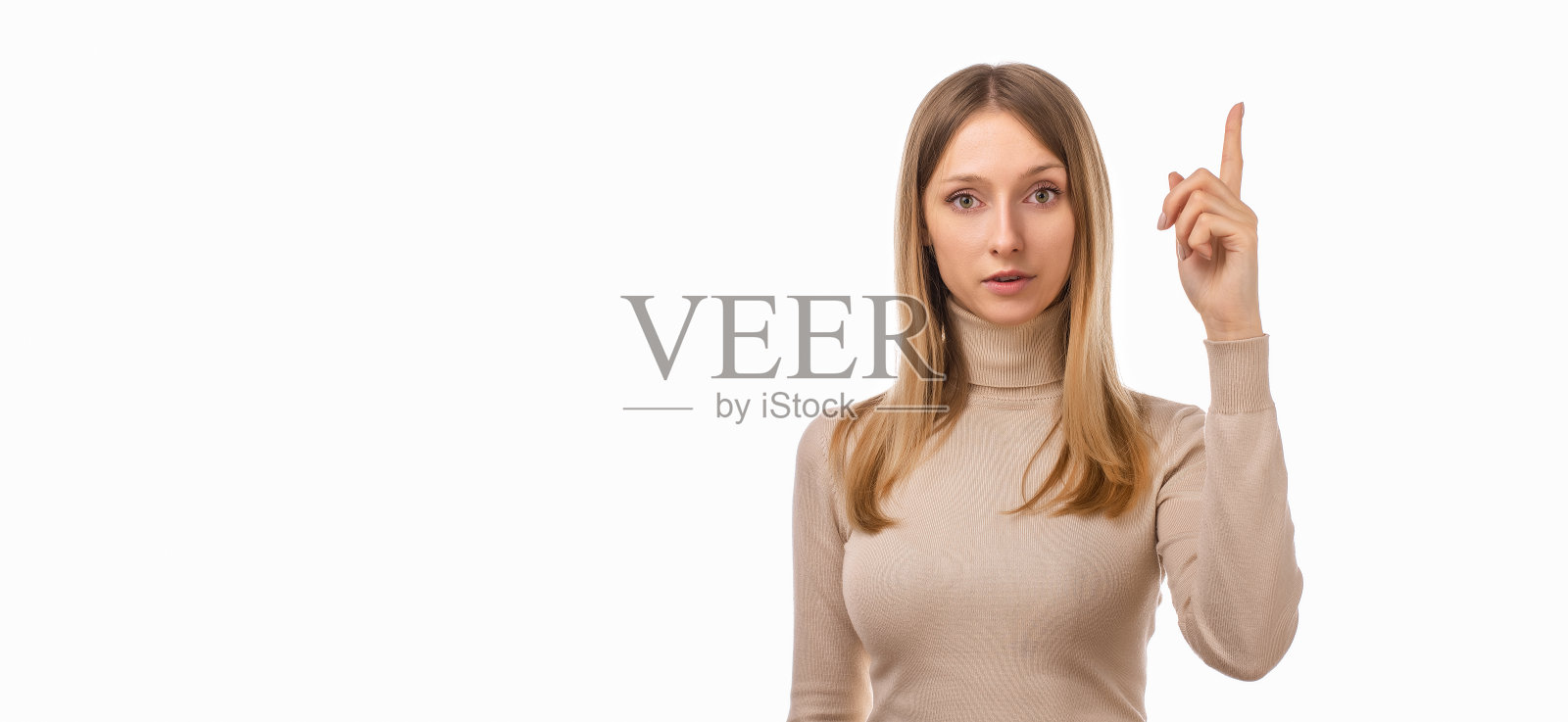 严肃的年轻金发女人伸出食指的肖像。女孩举起手指，说:请注意。广告的地方照片摄影图片