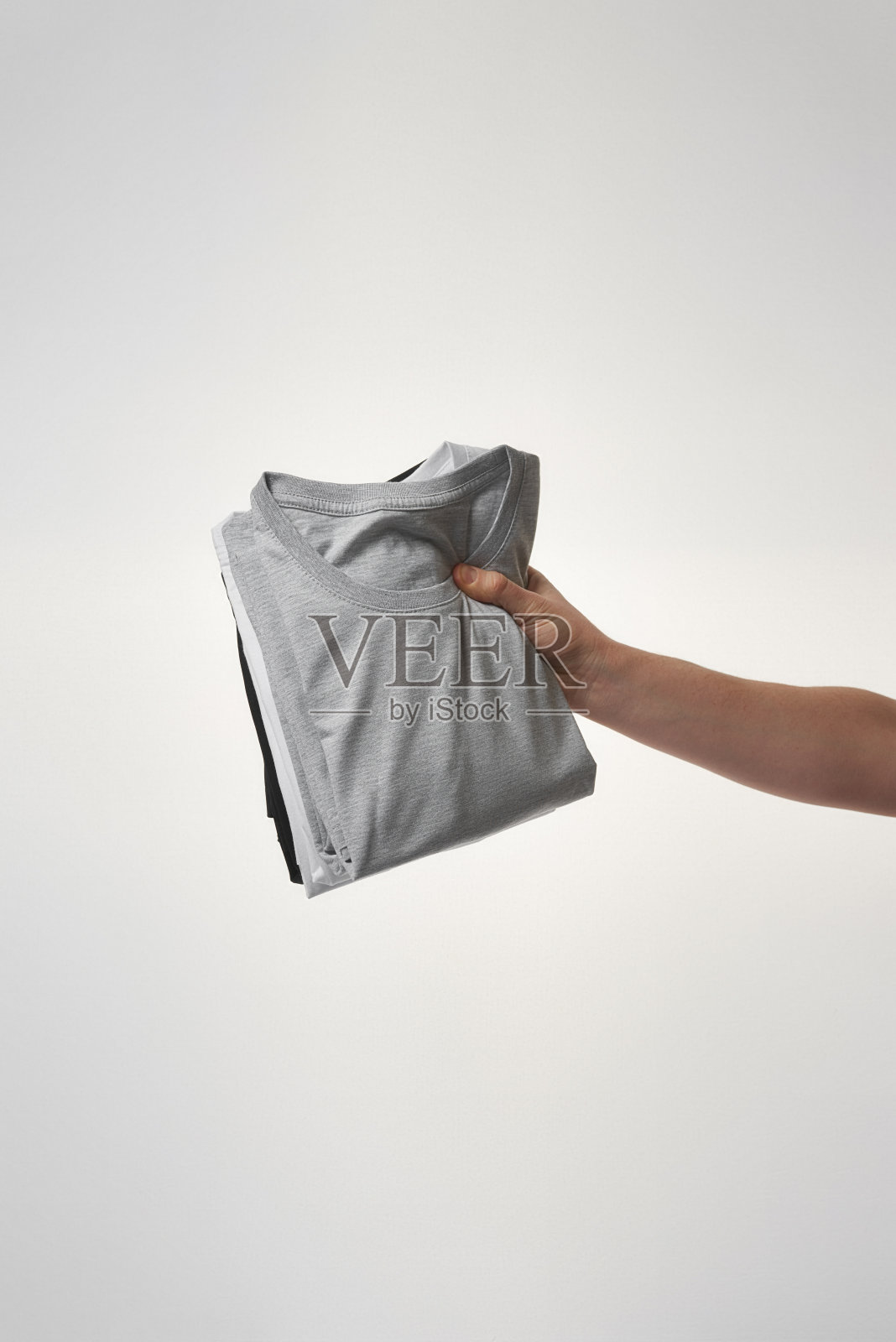 灰色背景下，男性手拿一堆基本t恤照片摄影图片