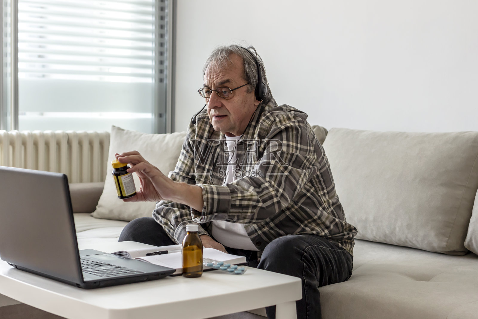 老人拿着他的日常药物，同时与医疗保健人员视频通话。照片摄影图片