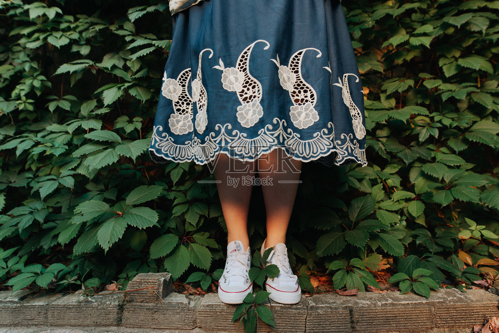 女腿在运动鞋在蓝色的裙子在草地的背景照片摄影图片