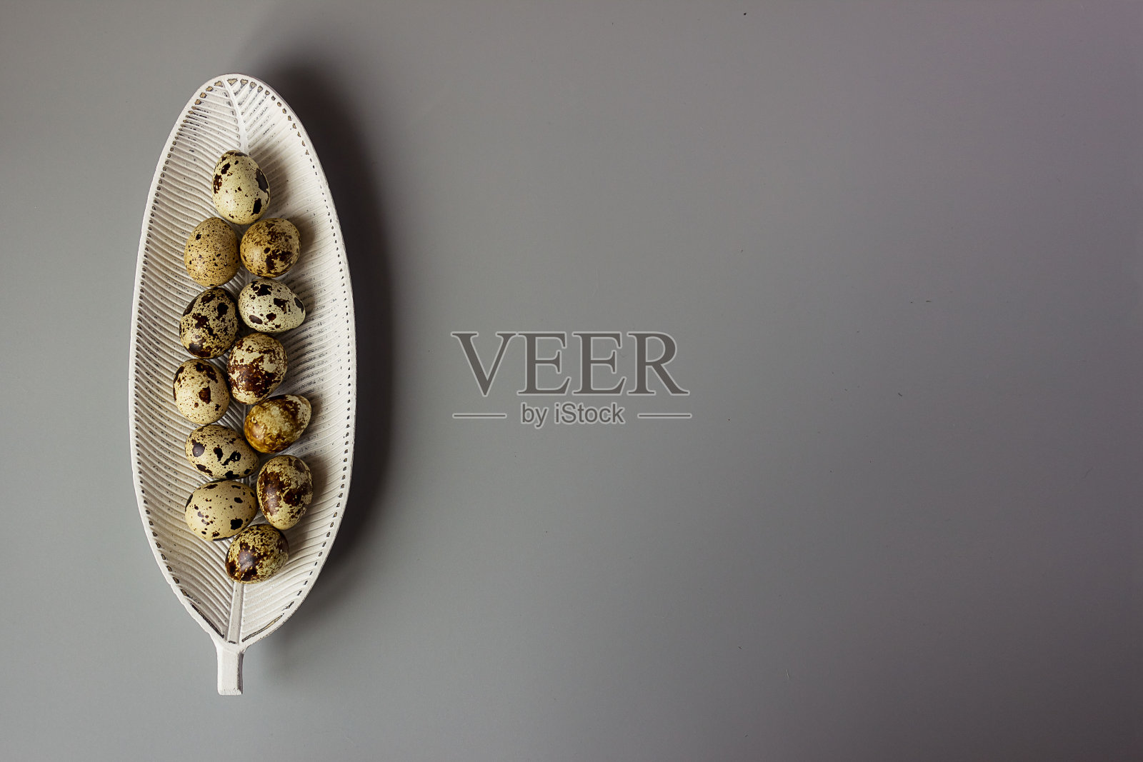 鹌鹑蛋放在叶子形状的盘子里，极简主义。优雅的复活节背景，文字的地方，复制空间照片摄影图片