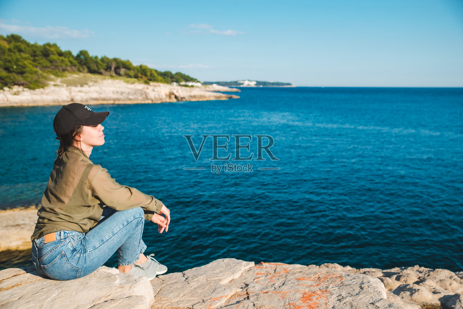 年轻漂亮的女人坐在悬崖上看着大海照片摄影图片