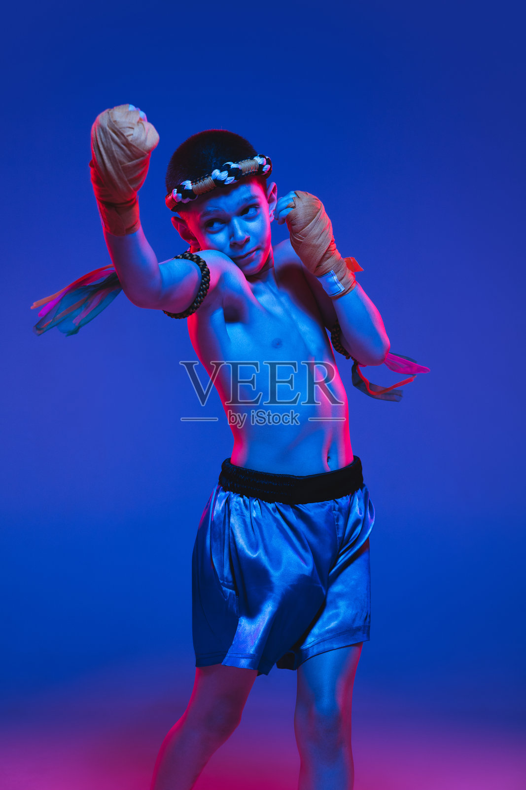 年轻的男孩泰国拳击手训练在霓虹灯的蓝色背景。照片摄影图片