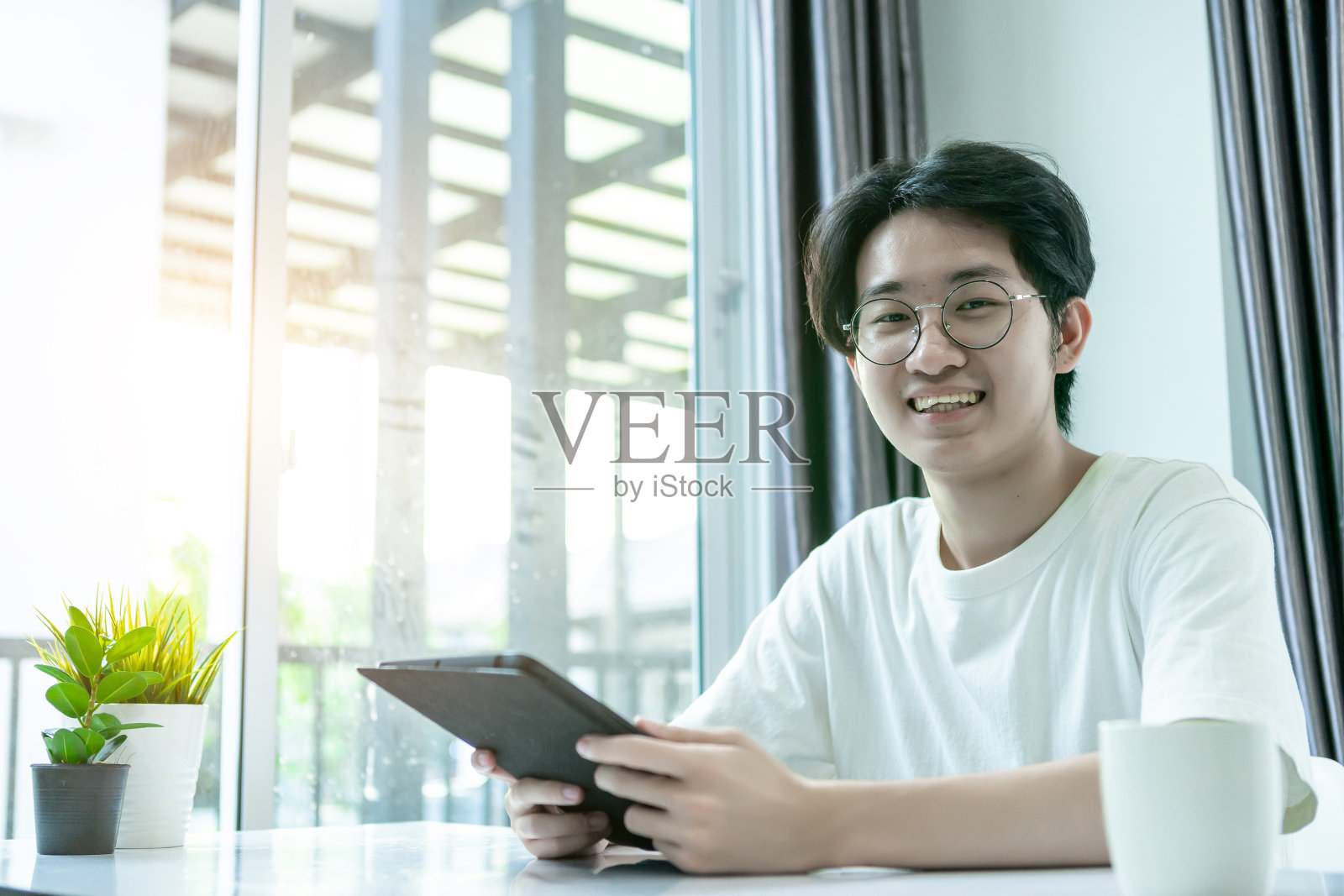 居家工作的亚洲男子，在新冠肺炎疫情下使用笔记本电脑和平板电脑，喝咖啡。她在隔离室工作在家工作的概念。照片摄影图片