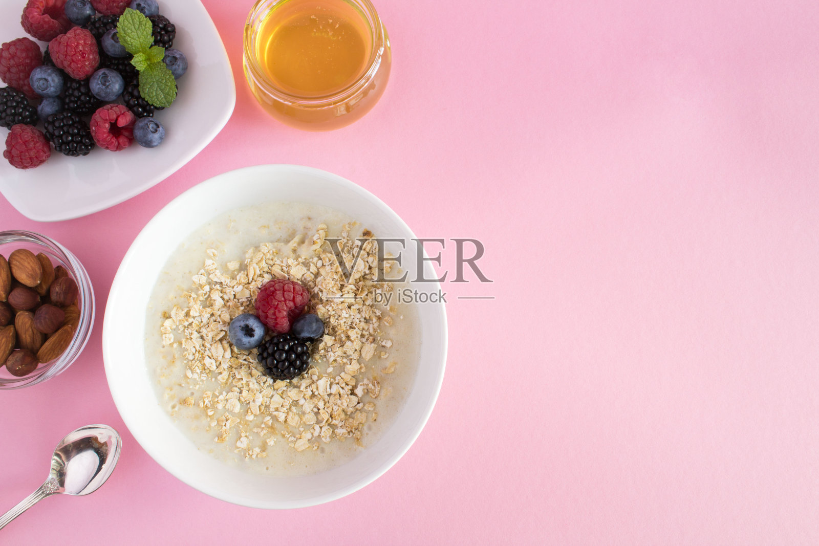 早餐:粉红色背景上有浆果、蜂蜜和坚果的燕麦粥。前视图。副本的空间。照片摄影图片