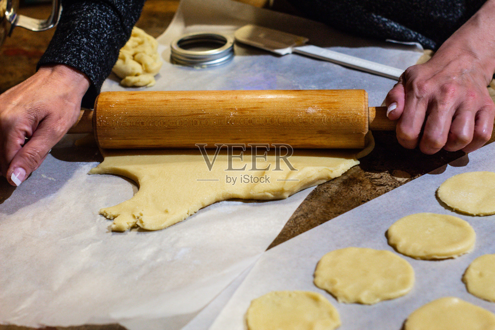 女人的手用擀面杖擀出甜饼面团并切出形状。照片摄影图片