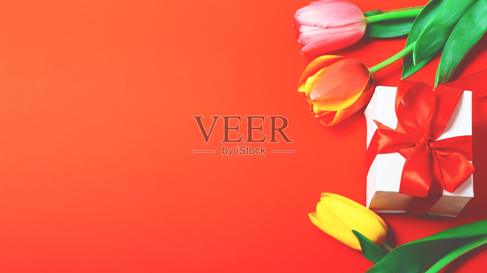 彩色的花束，春天的鲜花郁金香与礼盒在橙色的背景。复活节和春天的贺卡。本空间照片摄影图片