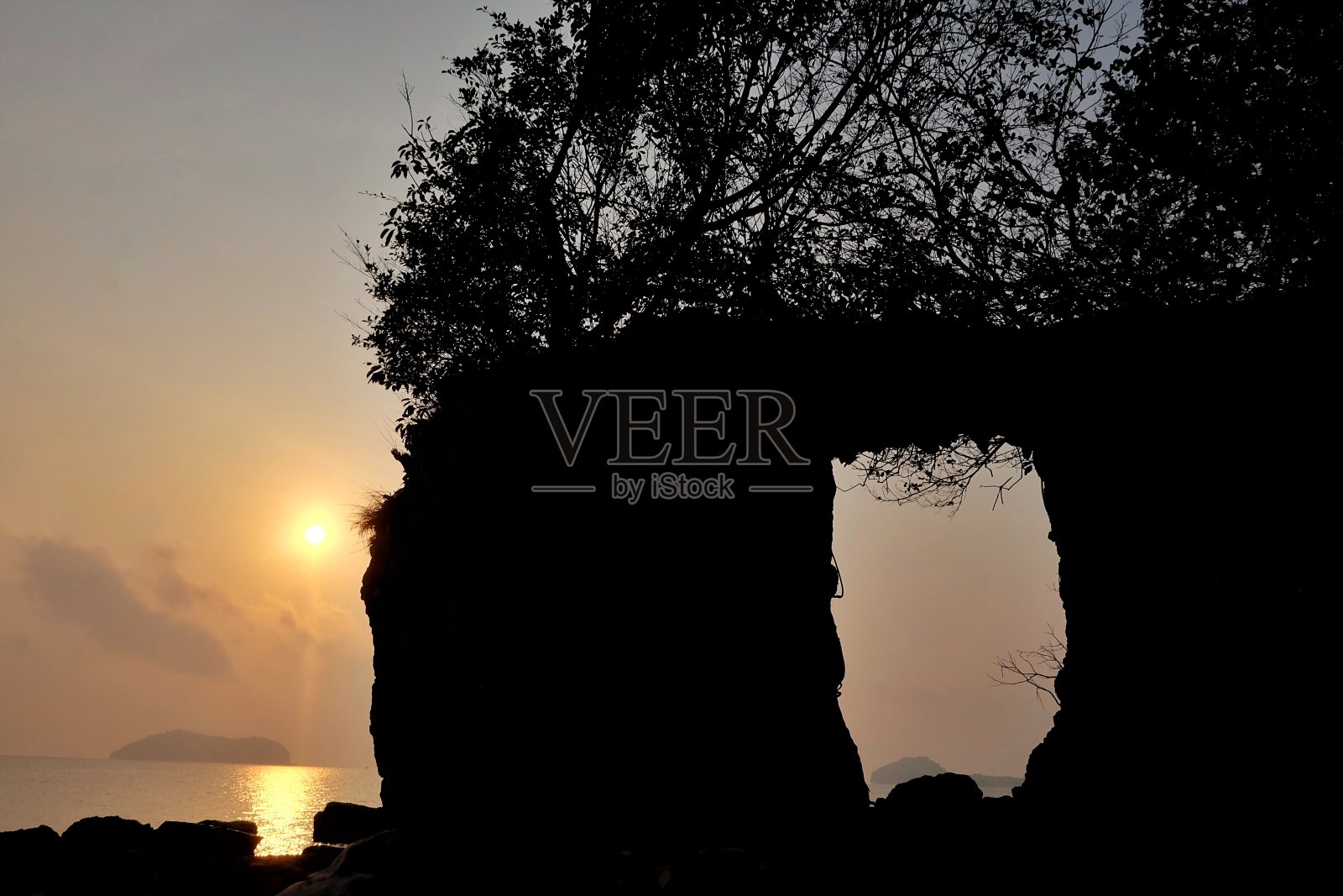 日出在早晨与金色的光在海水和一个巨大的岩石门口的影子照片摄影图片