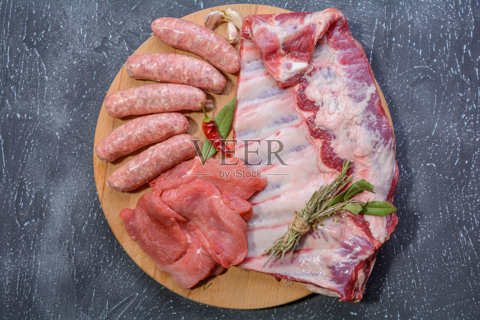 生的肉类产品。烧烤猪肋排，牛排，烤香肠，肉末，用香料装饰在圆形的木砧板上。平面布局。有选择性的重点。照片摄影图片