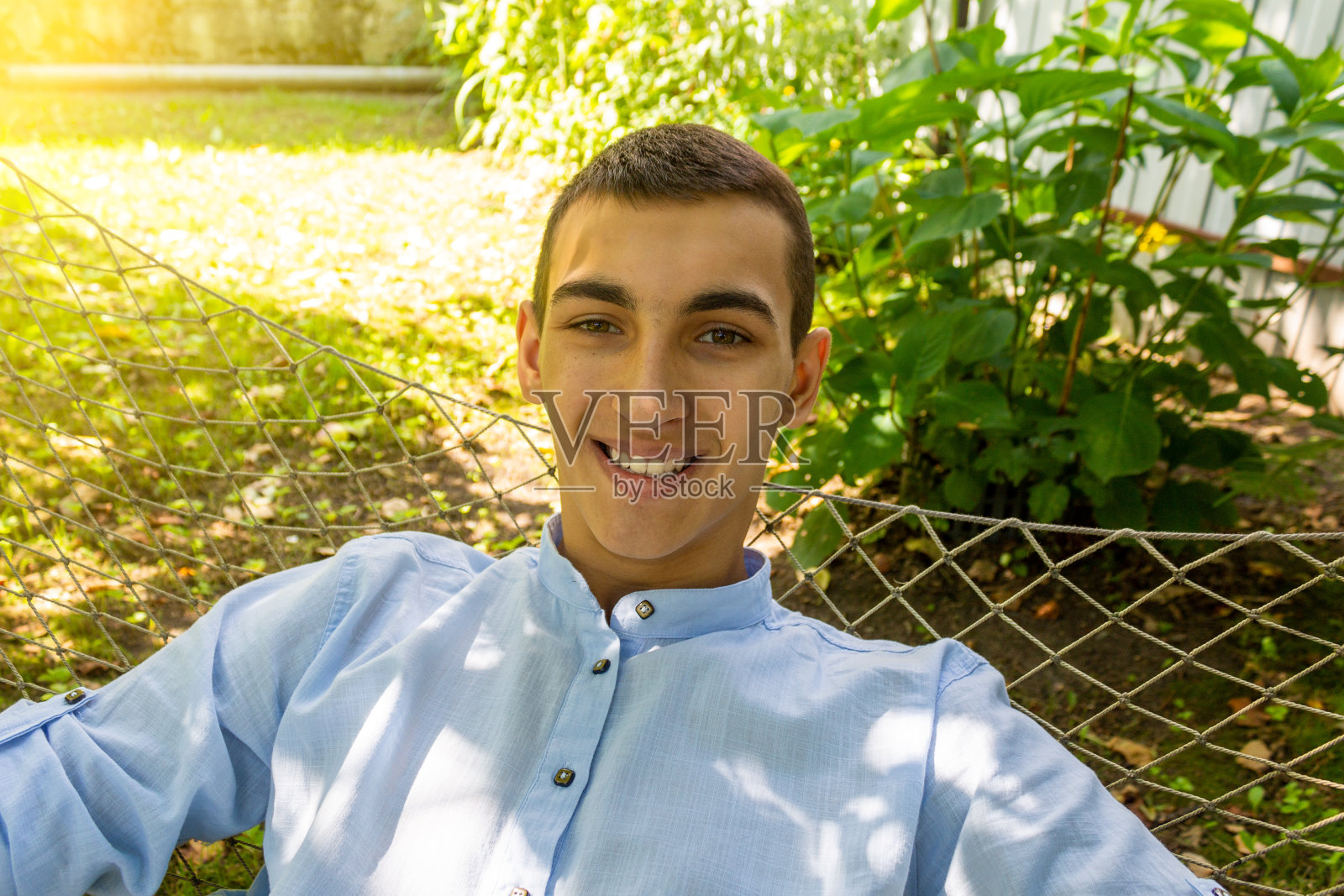 这是一个阳光明媚的夏日，一个微笑着的年轻帅哥躺在吊床上的自拍照照片摄影图片