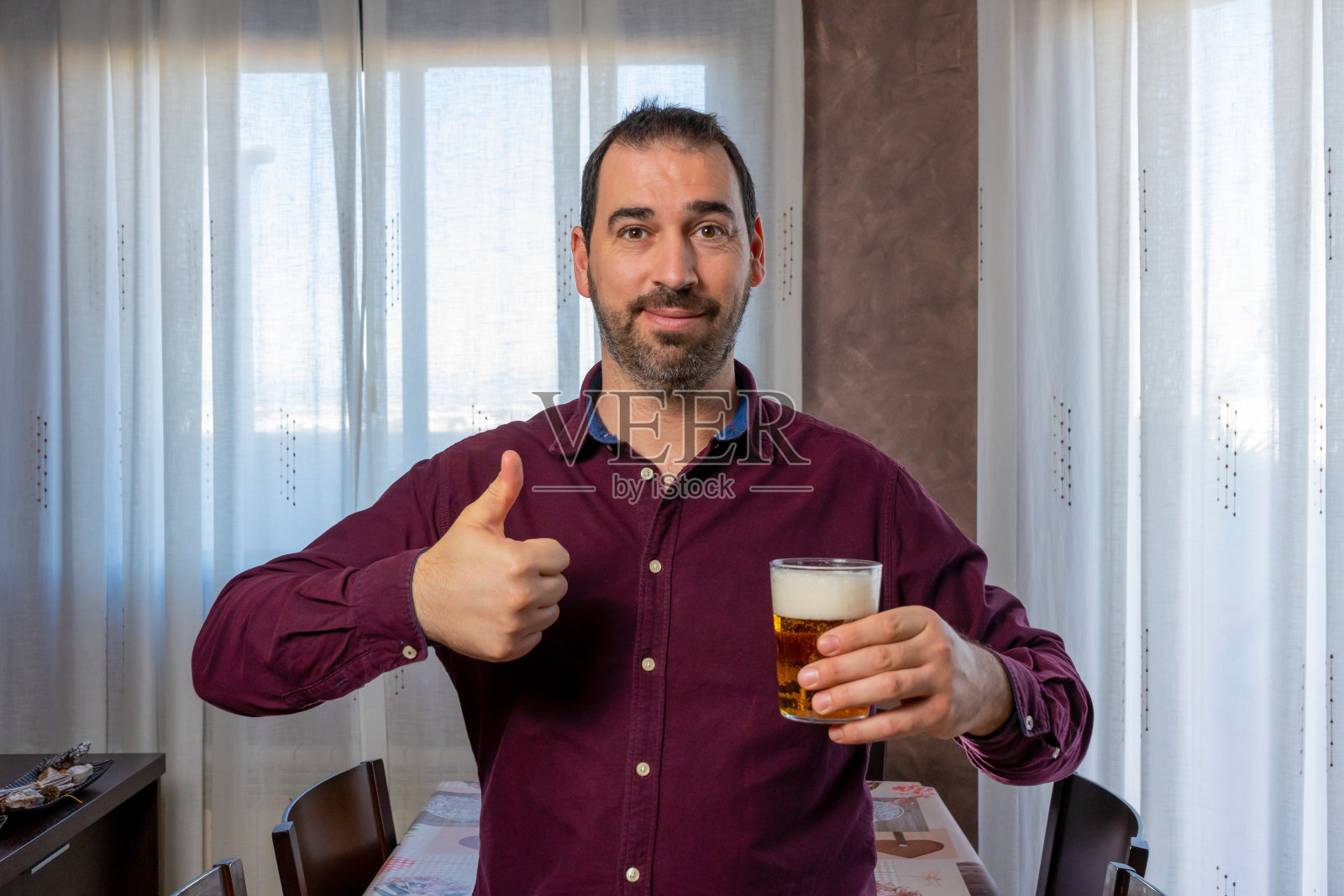 穿着紫色衬衫，满脸胡须，笑容可掬，大拇指翘着，另一只手拿着啤酒照片摄影图片