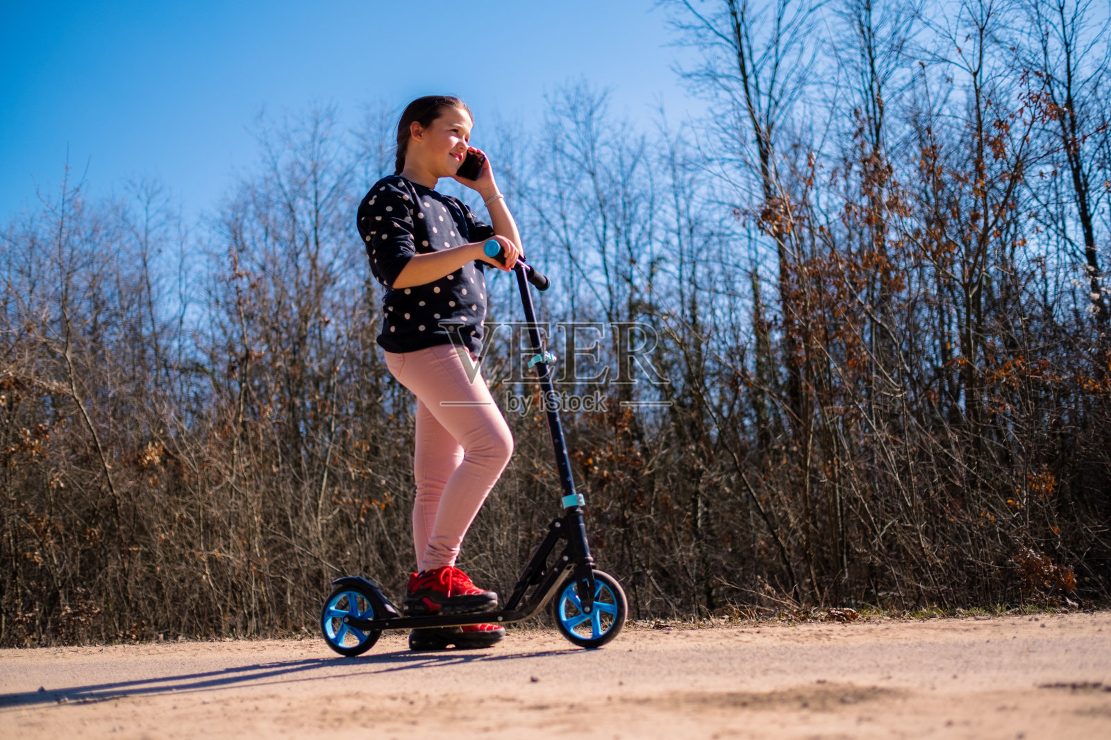 长头发的小女孩站在踏板车上打电话照片摄影图片