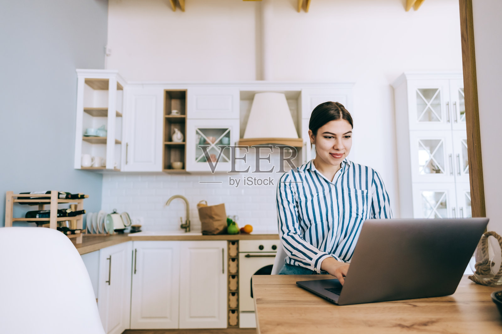 一个年轻的白人女人在用笔记本电脑，坐在厨房里。照片摄影图片