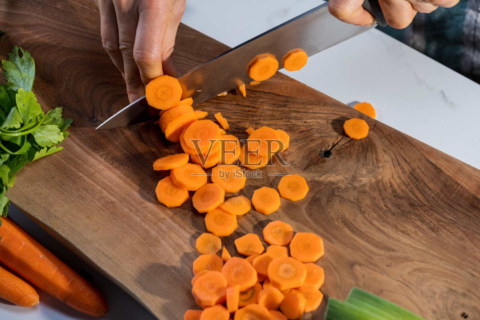 男子用手在木板上切橘子鲜胡萝卜。在厨房使用根茎类蔬菜配料。照片摄影图片