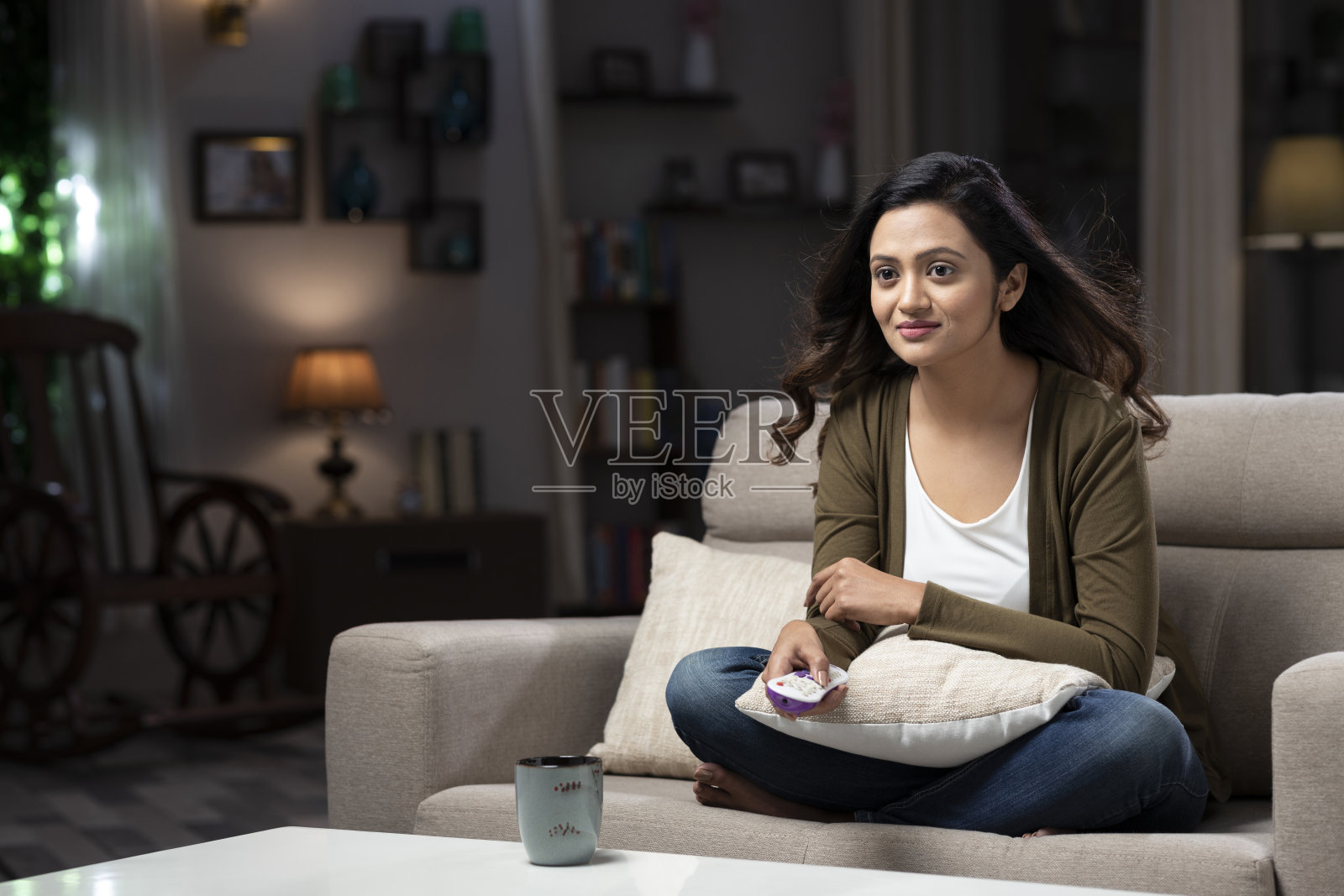 年轻的印度女人坐在沙发上看电视，笑着享受:-库存照片照片摄影图片