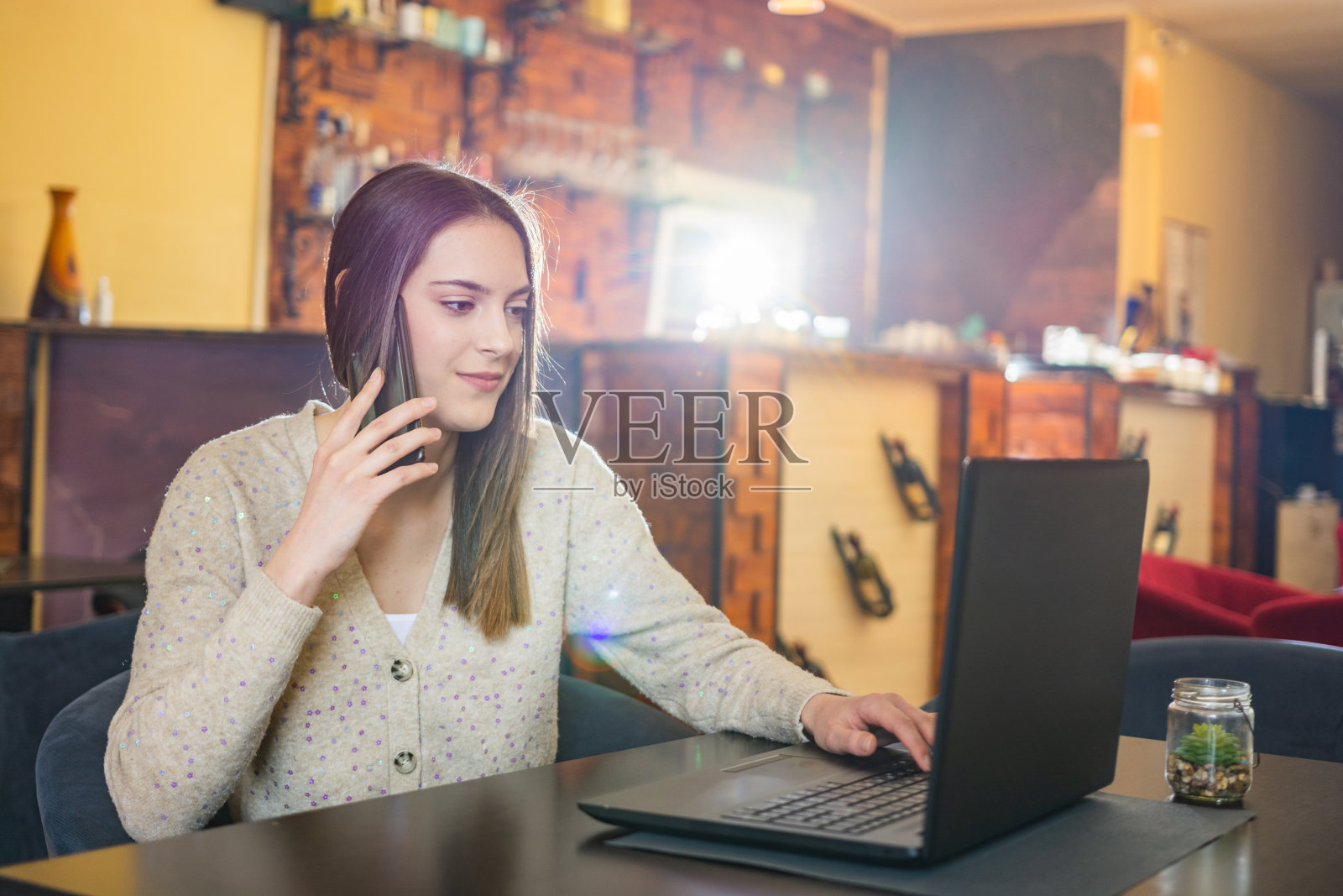 一个年轻女子正在酒吧里一边讲手机一边看笔记本电脑照片摄影图片