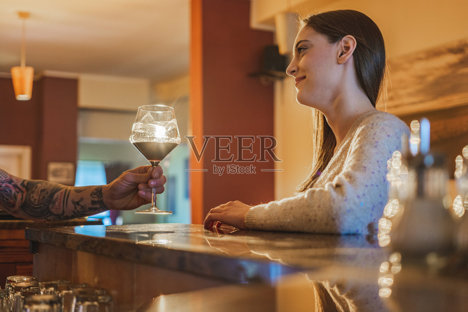 一位快乐的年轻女子坐在吧台前，酒保正递给她一杯酒照片摄影图片
