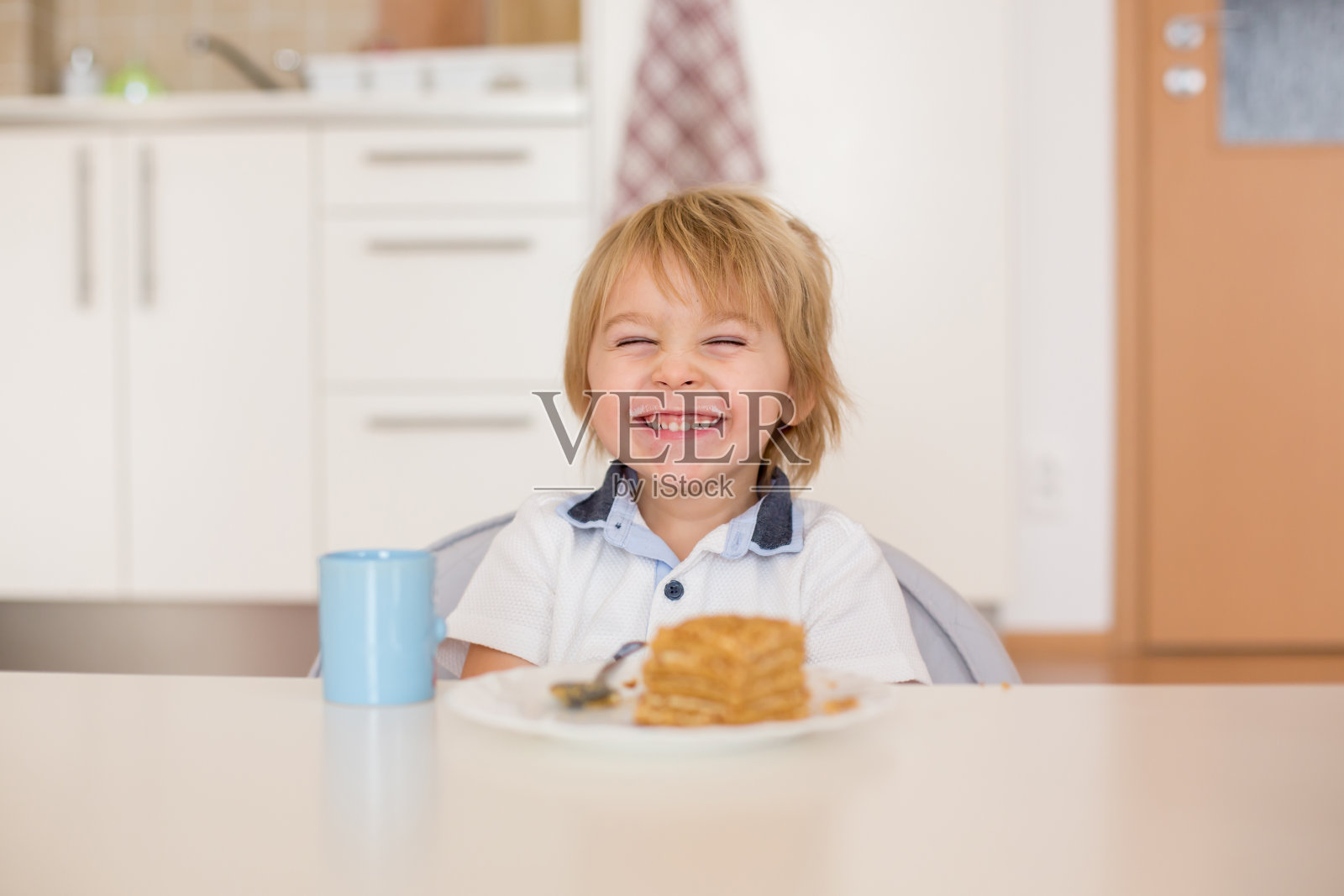 可爱的学龄前男孩，金发碧眼的孩子，在家里吃蛋糕喝牛奶照片摄影图片