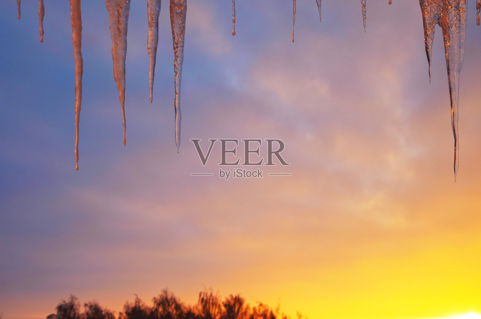 在夕阳和夕阳的背景上挂着冰柱。照片摄影图片