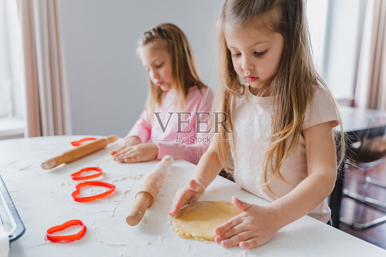 小女孩们，姐妹们在为情人节做自制的心形饼干。情人节。礼物，给妈妈的惊喜。红色模具，擀面杖，面粉，面团。手工家庭，带孩子的面包店照片摄影图片