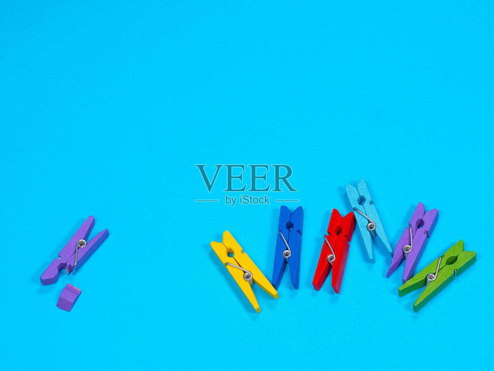 蓝色背景下的断腿木制紫色衣夹照片摄影图片