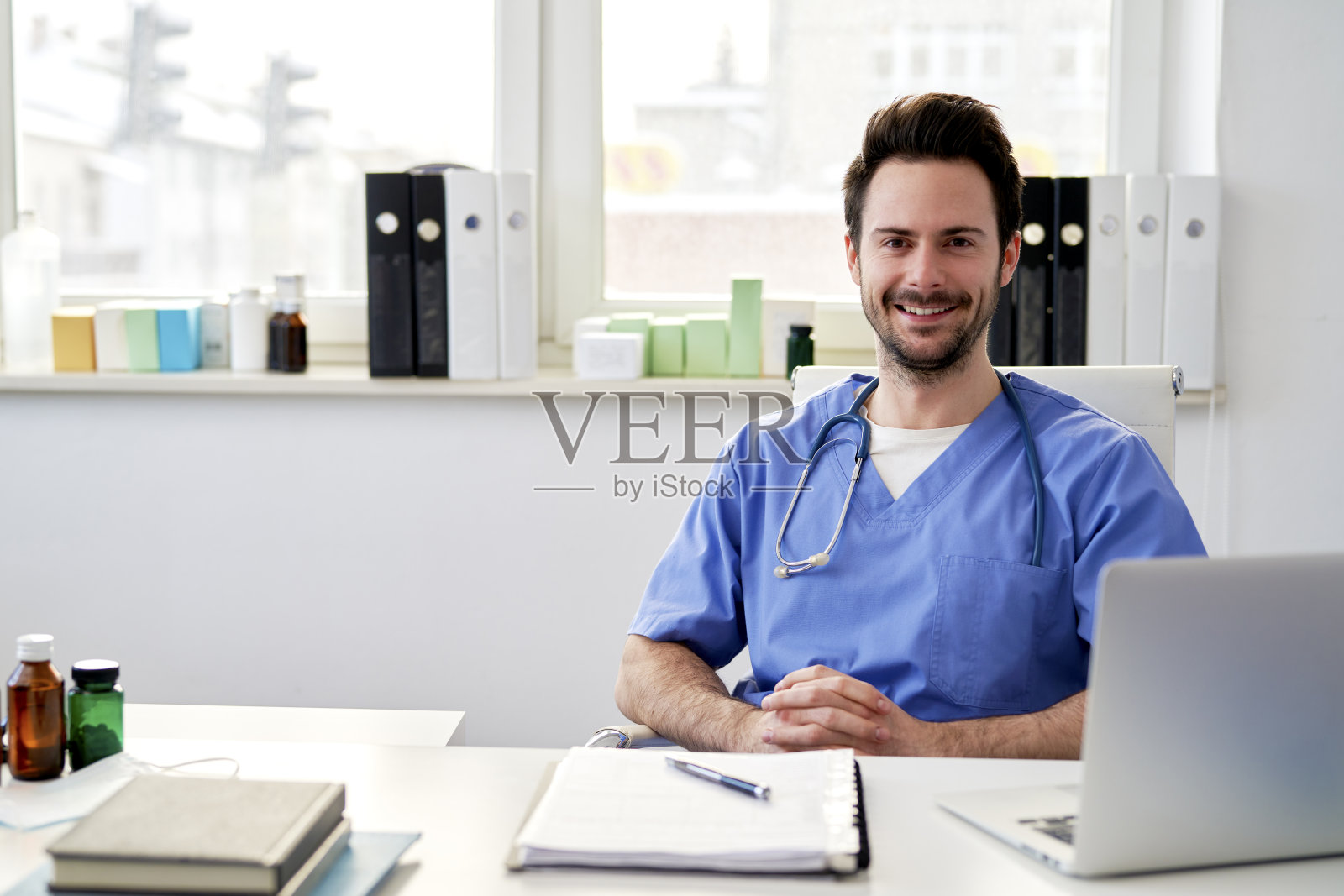 年轻快乐的医生坐在医生的办公室里照片摄影图片