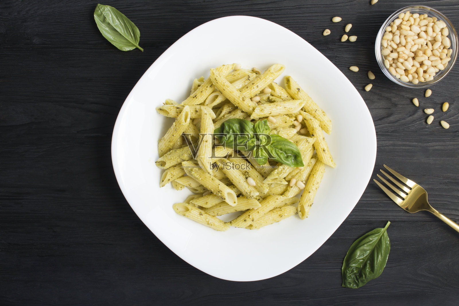 黑木背景上的白色盘子里放着香蒜沙司和松子的意大利面。前视图。照片摄影图片