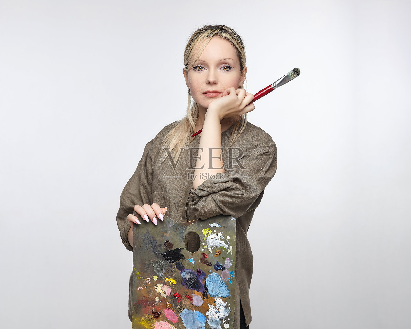 在一个白色背景的工作室里，年轻的女艺术家拿着调色板和画笔摆姿势照片摄影图片