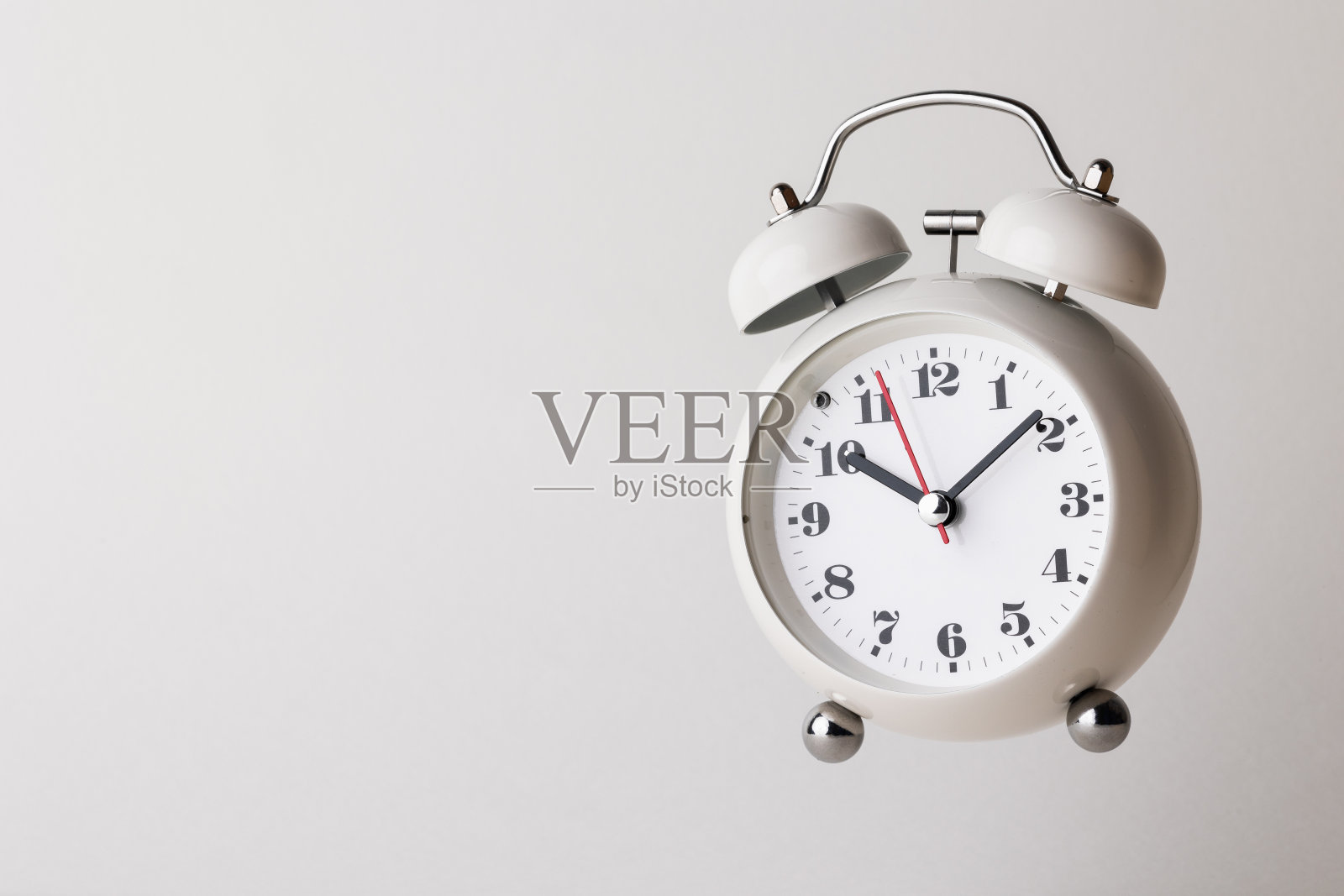 白色的小闹钟，黑色的数字，设定时间为10点10分，放在一张白色的桌子上。照片摄影图片