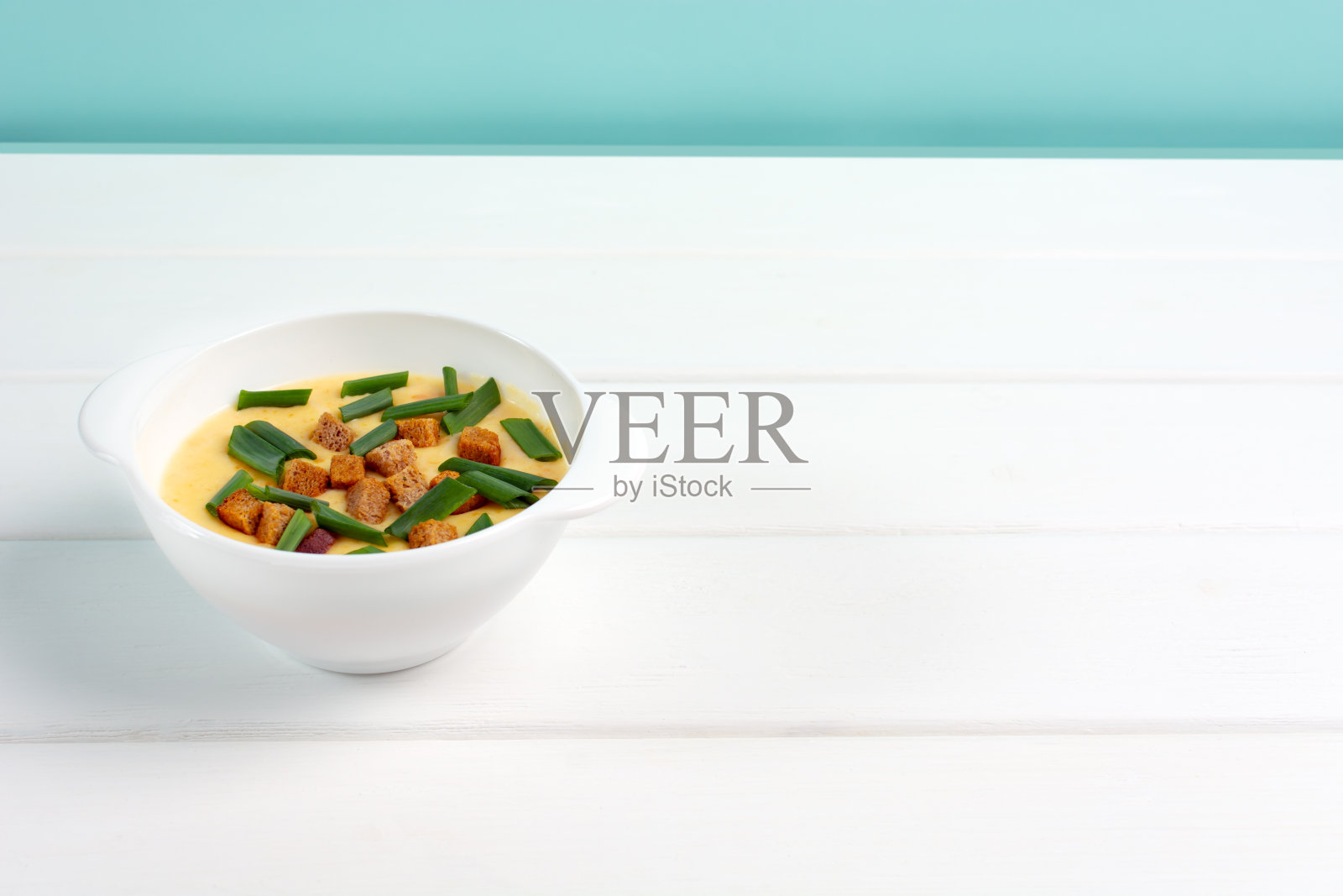 白色的桌子上，白色的盘子里盛着奶酪汤。青绿色的背景。副本的空间。照片摄影图片