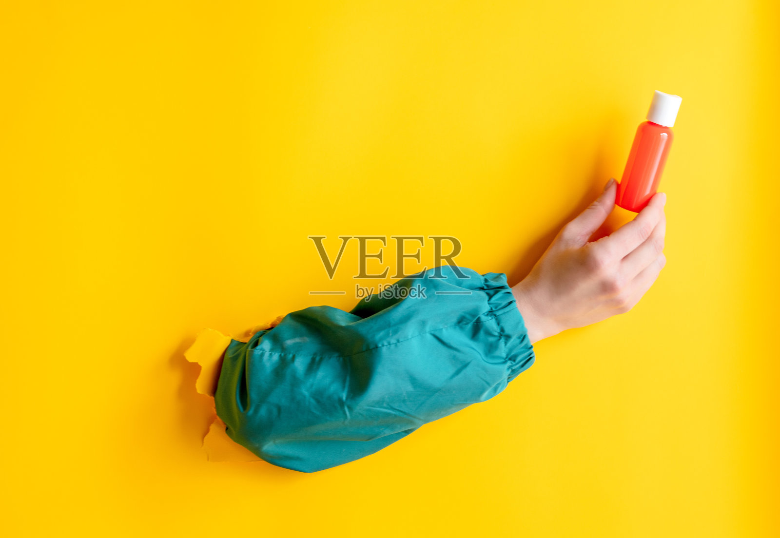 女性手握化妆品瓶上黄色的背景。照片摄影图片