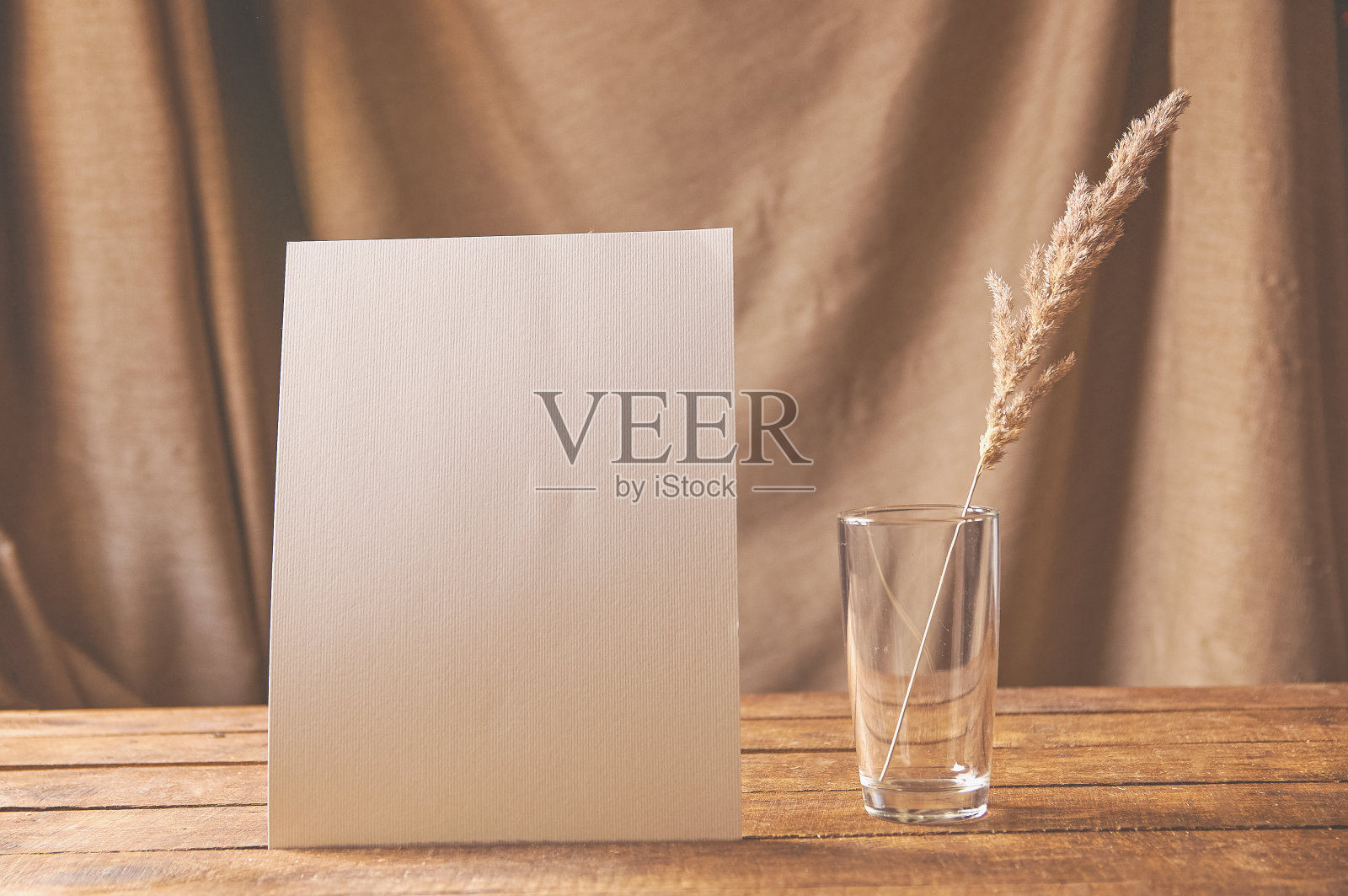 桌上放着一张白纸，上面有一个装着干花的玻璃杯。用于设计展示或作品集。照片摄影图片